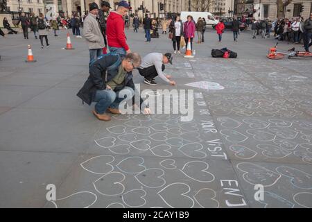 Touristen sahen Schreiben in Herzen gezeichnet mit weißer Kreide auf dem Bürgersteig des Trafalgar Square, London, Großbritannien von Straßenmusikern. Stockfoto