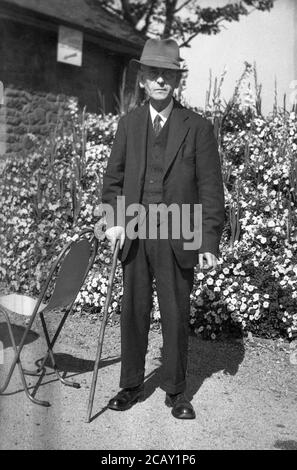 1940er Jahre, historisch, ein älterer englischer Gentleman, elegant gekleidet in einem dreiteiligen Anzug und Hut, der draußen auf seinem Stock lehnte, England, Großbritannien. Stockfoto