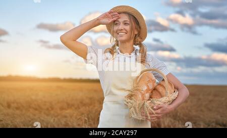 Frau Bäcker hält Weidenkorb Brot Öko-Produkt Frau Landwirt Stehende Weizen landwirtschaftlichen Bereich Backen kleine Unternehmen Kaukasischen Person gekleidet st Stockfoto