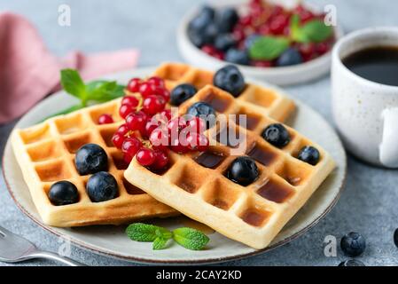 Belgische Waffeln mit Beeren, quadratische Form. Süße Waffeln zum Dessert mit einer Tasse schwarzem Kaffee Stockfoto