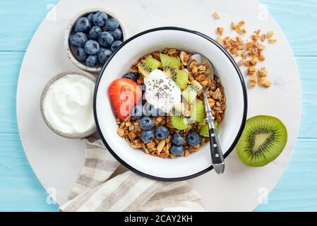 Frühstücksgranola Müslischale mit Obst und griechischem Joghurt auf einer Marmorplatte. Draufsicht. Konzept der Ernährung, saubere Ernährung, gesunde Lebensweise Co Stockfoto