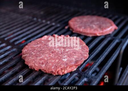 Rohes Rindfleisch Burger mit einer Prise Salz und schwarzem Pfeffer auf dem Grill. Zubereitetes Fleisch zum Grillen.Rohe Burger Cutlets. Runde Hacksteaks aus rohem Hackfleisch Stockfoto