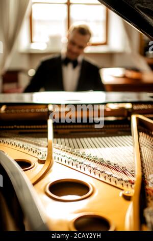 Nahaufnahme des klassischen Klavierinstruments, junger Mann in Anzug, der darauf spielt, klassische Musik aufführt Stockfoto