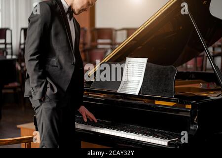 Porträt eines jungen kaukasischen Mannes in formell eleganten Anzug neben Klavier, professionelle Musiker nach der Aufführung Stockfoto