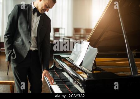 Porträt eines jungen kaukasischen Mannes in formell eleganten Anzug neben Klavier, professionelle Musiker nach der Aufführung Stockfoto