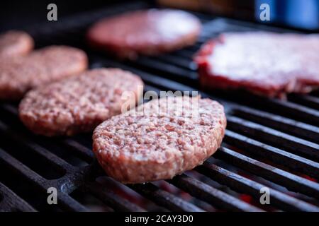 Rohes Rindfleisch Burger mit einer Prise Salz und schwarzem Pfeffer auf dem Grill. Zubereitetes Fleisch zum Grillen.Rohe Burger Cutlets. Runde Hacksteaks aus rohem Hackfleisch Stockfoto