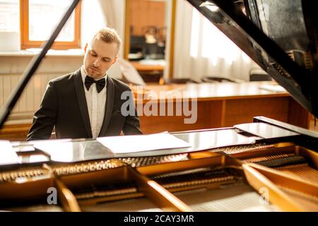 Junge gut aussehende kaukasischen Mann in formell eleganten Anzug anmutig spielen Klavier. Professionelle Pianist führen klassische Musik Stockfoto