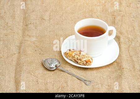 Tasse Tee, Müsliriegel und Teesieb auf Sacktuch Stockfoto