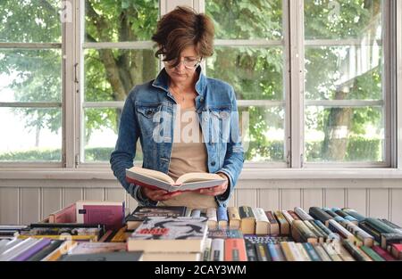 Nahaufnahme einer stilvollen kaukasischen Frau mittleren Alters, die ein Buch liest Im alten Vintage-Buchladen Stockfoto