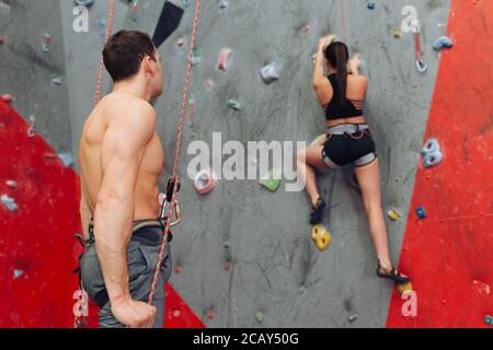 Starker junger Mann mit Blick auf schlanke Klettermädchen im Sportzentrum. Stockfoto