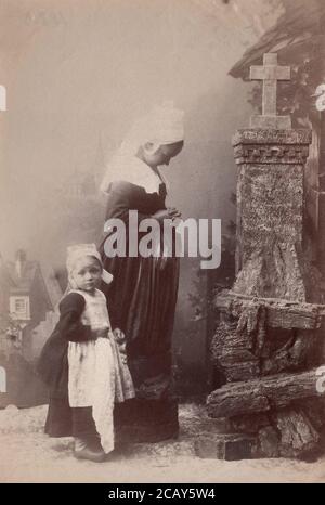 Eine schwangere Frau und ein Kind beten vor dem Kreuz. Holland, 1880 von einem alten Druck. Stockfoto