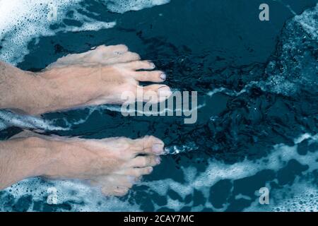 Männliche Füße am schwarzen Sandstrand Stockfoto