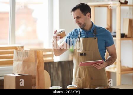 Waist up Porträt von reifen Mann trägt Schürze Verpackungsaufträge, während Sie am Holztisch stehen, Lebensmittel-Lieferservice-Mitarbeiter, Kopierer Raum Stockfoto