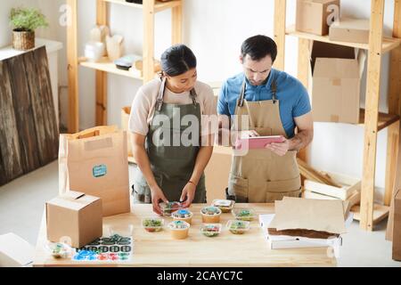 Hochwinkel-Porträt von zwei Arbeitern tragen Schürzen Verpackungsaufträge an Holztisch in Food Delivery Service, kopieren Raum Stockfoto