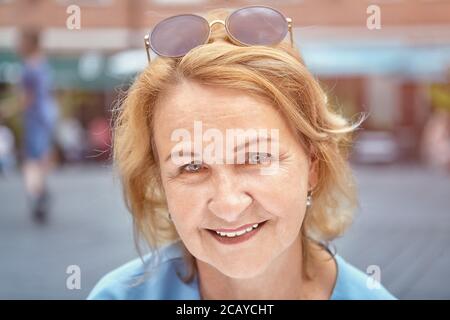Portrait von gealterten weißen attraktiven Dame über 60 Jahre alt im öffentlichen Park. Sie lächelt und sieht aktiv, charmant und freundlich Frau. Sie trägt eine Sonnencreme Stockfoto