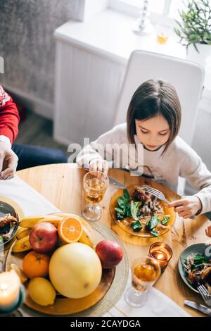 Top-Winkel-Ansicht, liebenswert Tochter mit Abendessen mit Verwandten. Kind schmeckt die gebratene hausgemachte türkei Stockfoto