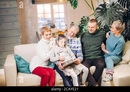 Erweiterte freundliche Familie mit Blick auf photo.pleasant Erinnerung aus der Kindheit. Drei Generationen auf dem Sofa Stockfoto