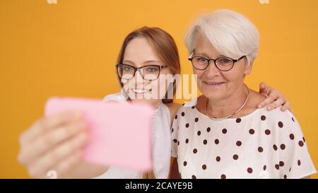 Ältere und junge Frau, die Selfies auf orangefarbenem Hintergrund macht. Hochwertige Fotos Stockfoto