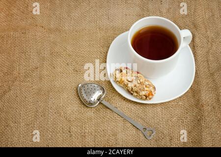 Tasse Tee, Müsliriegel und Teesieb auf Sacktuch. Draufsicht Stockfoto