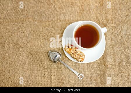 Tasse Tee, Müsliriegel und Teesieb auf Sacktuch. Draufsicht Stockfoto