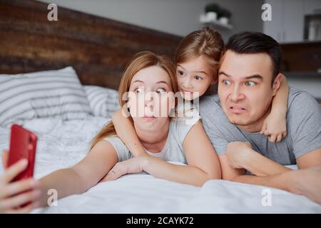 Lassen Sie uns Selfie, Foto. Portrait der schönen lustigen Familie Selfie mit Tochter, Mädchen mit Casuals auf dem Bett zu Hause Stockfoto