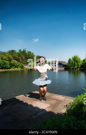 Eine glückliche chinesin, die an einem wolkenlosen Tag in der Provinz Zhejiang in der Nähe eines Teiches in der malerischen Gegend des East Lake in Shaoxing China springt und Spaß hat. Stockfoto