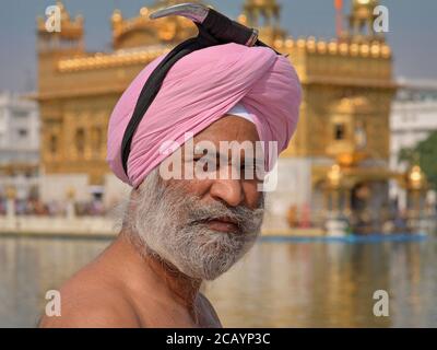 Der ältere indische Sikh-Anhänger bereitet sich auf ein Bad im heiligen „Teich des Nektars“ rund um den Goldenen Tempel vor und sichert seinen Dolch auf seinem Turban. Stockfoto