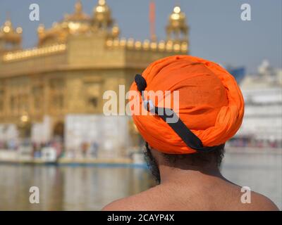 Indischer Sikh-Mann mit zeremoniellem Dolch (Kirpan) in seinem orangen Turban blickt auf den Goldenen Tempel im Hintergrund. Stockfoto