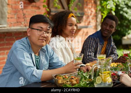 Portrait von lächelnden asiatischen Mann genießen Abendessen mit Freunden im Freien und Blick auf die Kamera, während am Tisch sitzen während der Sommerparty, kopieren Raum Stockfoto