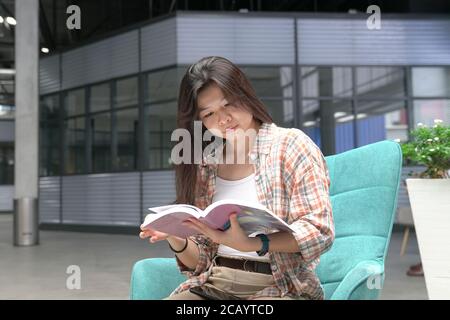 Asiatische Frau sitzt auf einem Stuhl und liest ein Buch Stockfoto