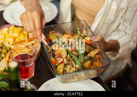 Nahaufnahme einer nicht erkennbaren Frau, die ein Gericht mit goldgerösteten Kartoffeln hält, während Sie das Abendessen mit Freunden und Familie im Freien genießen, Platz kopieren Stockfoto