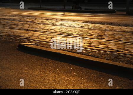 In der Nähe der Straßenbahnhaltestelle Ohrada in Prag, Tschechien, spiegelt die Straße, auf der die Straßenbahnschienen stehen, die schönen orange/gelben Farben der untergehenden Sonne wider. Stockfoto