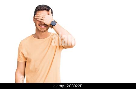 Hübscher junger Mann mit Bär trägt lässiges gelbes T-Shirt lächelnd und lachend mit Hand auf Gesicht, die Augen für Überraschung bedeckt. Blind Konzept. Stockfoto