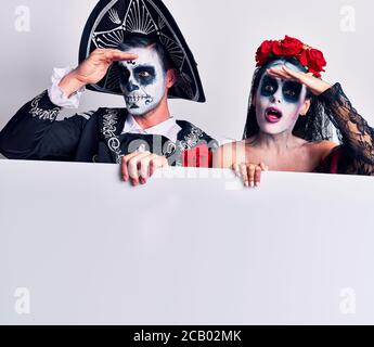 Junges Paar mit mexikanischem Tag der Toten Kostüm mit leerem leeren Banner sehr glücklich und lächelnd, weit weg mit der Hand über dem Kopf. Suchen Stockfoto