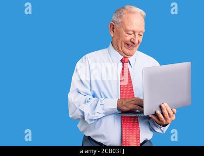 Senior stattlichen grauhaarigen Mann trägt Krawatte mit Laptop sieht positiv und glücklich stehen und lächeln mit einem selbstbewussten Lächeln zeigt Zähne Stockfoto