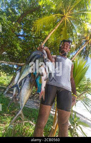 Der Mann hält eine Schnur tropischer Fische, die er mit einem Speer und Schnorchelausrüstung gefangen hat. Zu den Fischen gehören Silberjacken, Chirurgenfische, graue Kaiser und mehr. Stockfoto