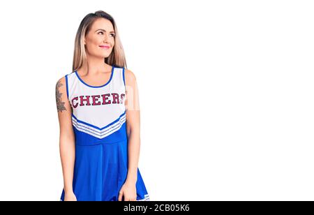 Junge schöne blonde Frau trägt Cheerleader Uniform lächelnd Blick auf die Seite und starrte weg denken. Stockfoto