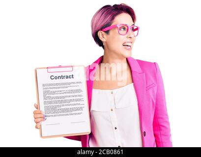 Junge schöne Frau mit rosa Haar hält Zwischenablage mit Vertrag Dokument Blick weg zur Seite mit Lächeln auf Gesicht, natürlichen Ausdruck. Lachen Co Stockfoto