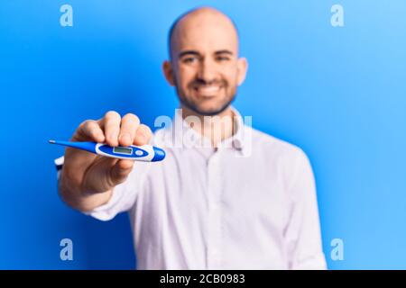 Junge gutaussehende Glatze Mann hält Thermometer positiv und glücklich stehend und lächelnd mit einem selbstbewussten Lächeln zeigt Zähne Stockfoto