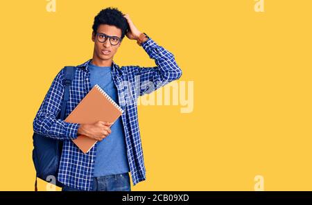 Junger afroamerikanischer Mann trägt Student Rucksack halten Buch verwirren und fragen sich über Frage. Unsicher mit Zweifel, Denken mit Hand auf hea Stockfoto