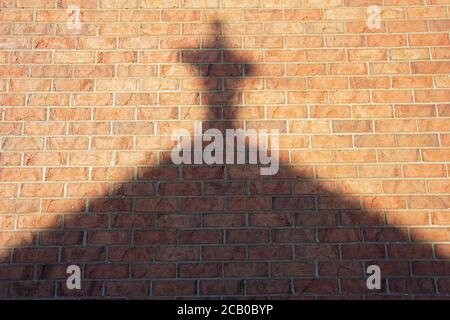 Kreuzreflexion an einer Wand und religiöses Symbol, spätnachmittags Licht auf einem Backstein Hintergrund. Stockfoto