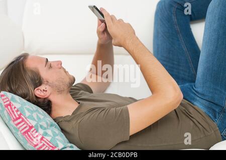 Nahaufnahme eines hübschen jungen Mannes, der sein Telefon benutzt, während er auf einem Sofa liegt. Entspannungs- und Kommunikationskonzept. Stockfoto