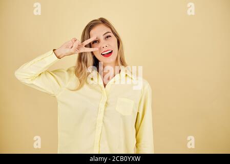 Studio-Porträt von ziemlich blonde junge Frau, die Frieden Geste Und lächelnd auf die Kamera Stockfoto