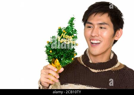 Studio Schuss von jungen schönen asiatischen Mann hält Happy New Jahrbaum und lächelnd isoliert vor weißem Hintergrund Stockfoto