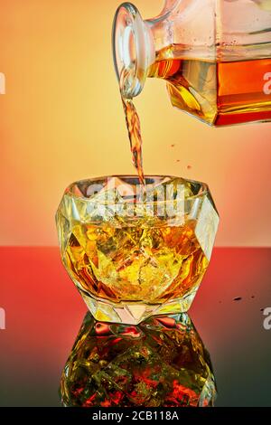 Gießen Luxus-Whiskey in ein Kristallglas mit Eis auf einem gradienten Hintergrund. Stockfoto