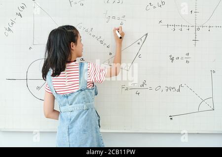 Smart Schulmädchen Schreiben auf Whiteboard bei der Lösung Geometrie Aufgabe in der Klasse, Blick von hinten Stockfoto