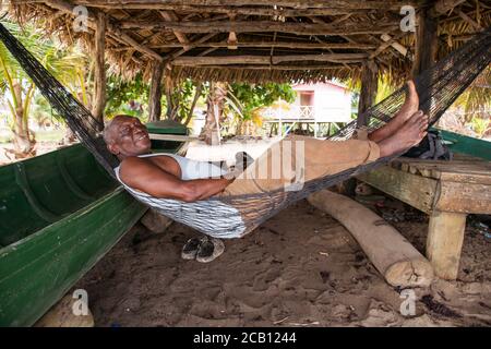 Hopkins / Belize - 10. Oktober 2016: Pensionierter belize-Mann, der in der Hängematte am Strand unter dem Schuppen in der Küstenstadt liegt Stockfoto