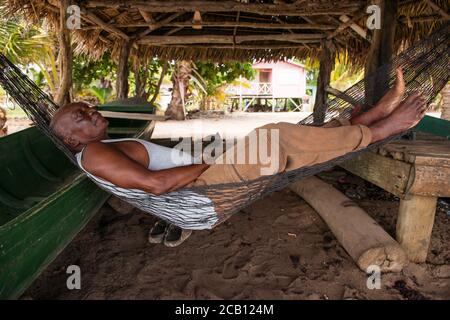 Hopkins / Belize - 10. Oktober 2016: Pensionierter belize-Mann, der in der Hängematte am Strand unter dem Schuppen in der Küstenstadt liegt Stockfoto
