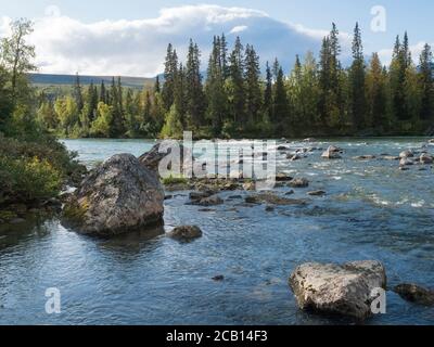 Wunderschöne nördliche Landschaft mit azurblauem Fluss Kamajokk, Bergen, Felsbrocken und Fichtenwald in Kvikkjokk in Schwedisch Lappland. Sommer sonnig Stockfoto