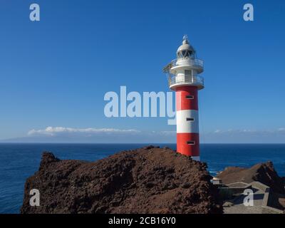 Blick auf den rot-weißen Leuchtturm am Kap Punta de Teno Im Westen Teneriffas kanarische Insel mit Lavagestein blaues Meer Und klaren Sommerhimmel Stockfoto